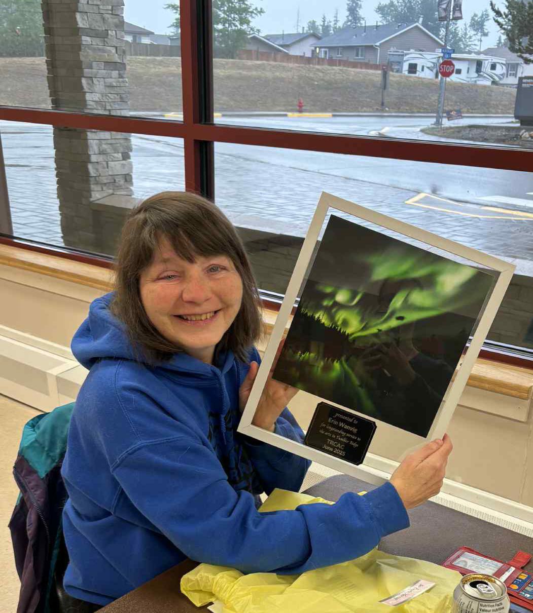 A woman in blue hooded sweater holds up a framed photo of the northern lights.