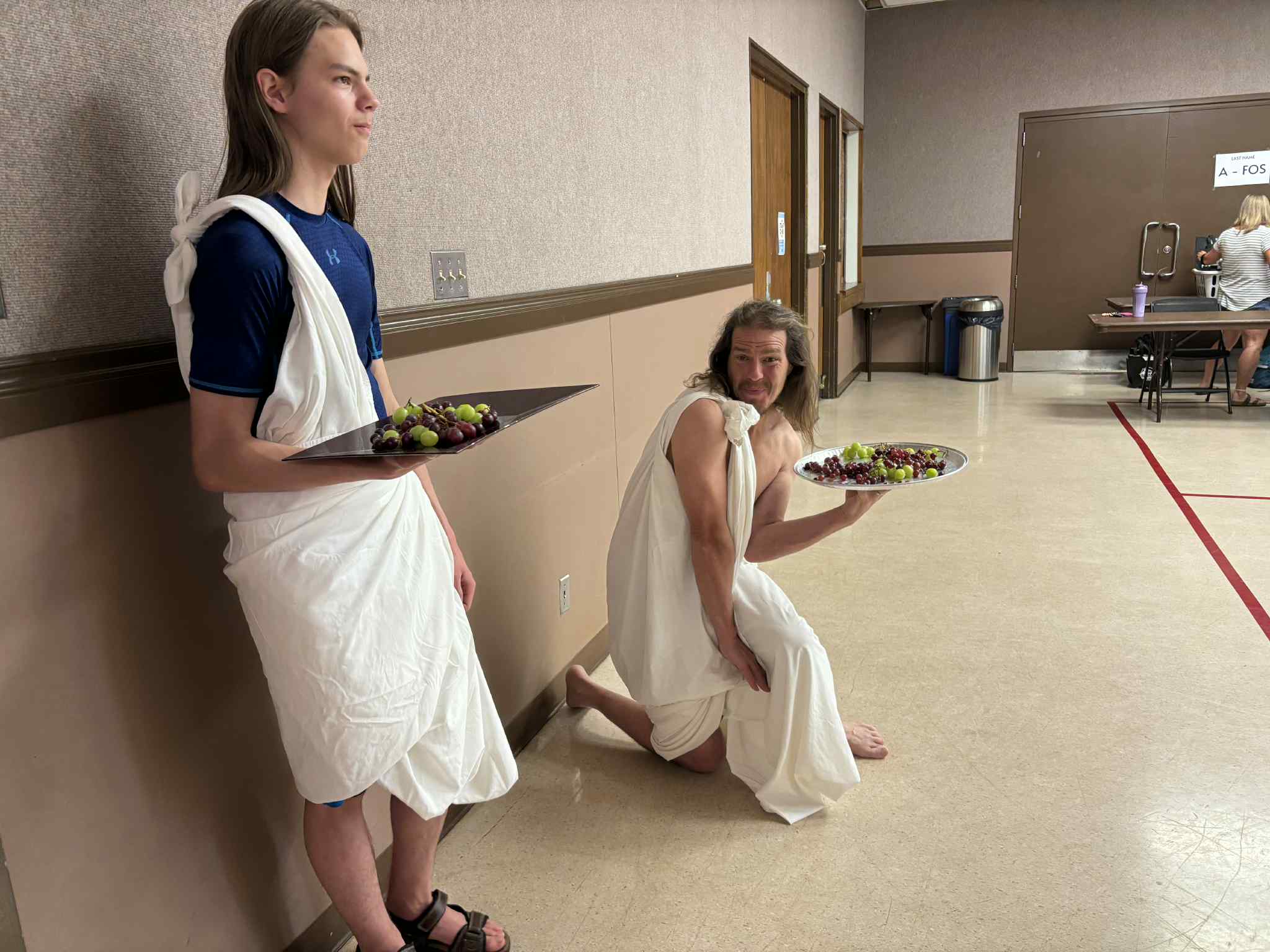TRCAC volunteers dressed in white togas hold out platters of green and red grapes. Photo contributed by Zena Conlin, TRCAC President (2025-26)